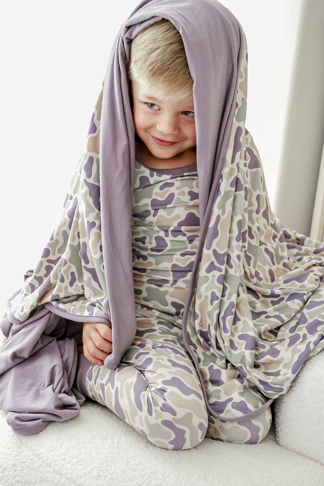 Toddler boy with camo cutie double-sided bamboo blanket draped over his head and shoulders, wearing matching camo pajamas