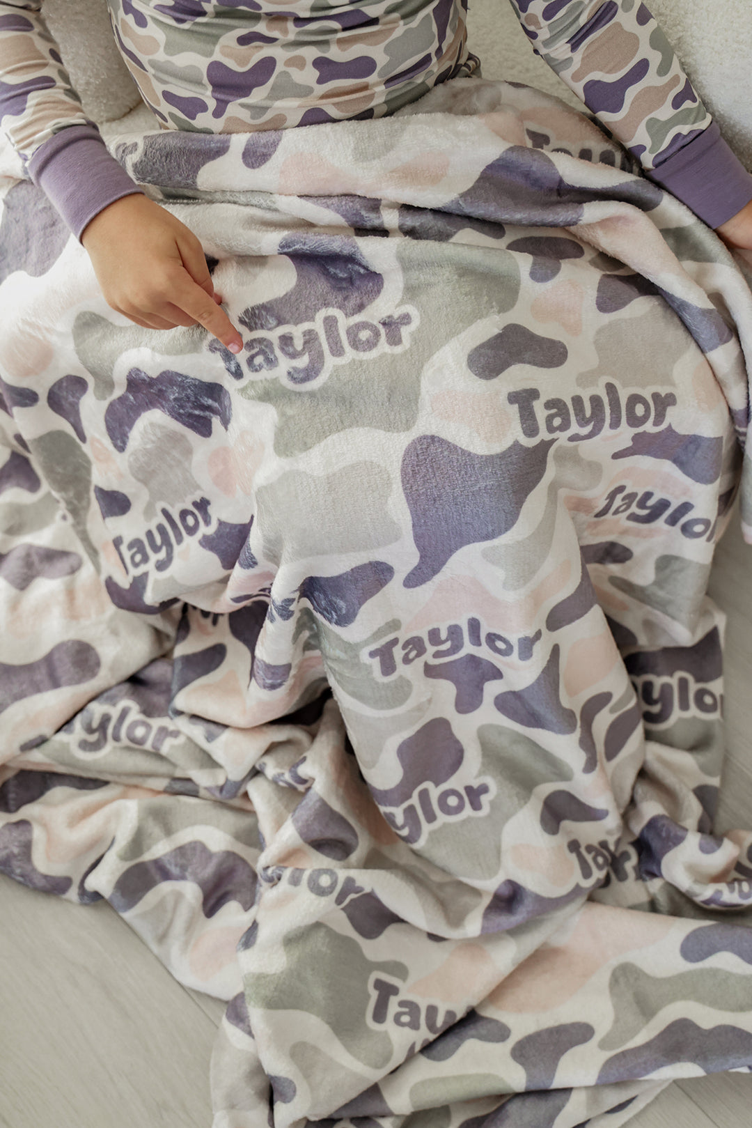 Close-up of child's hand pointing to custom name on personalized camo cutie kids blanket, child wearing matching camo pajamas