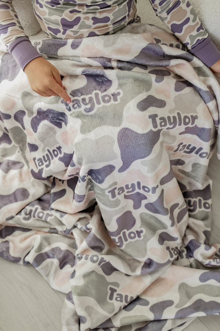 Close-up of child's hand pointing to custom name on personalized camo cutie kids blanket, child wearing matching camo pajamas