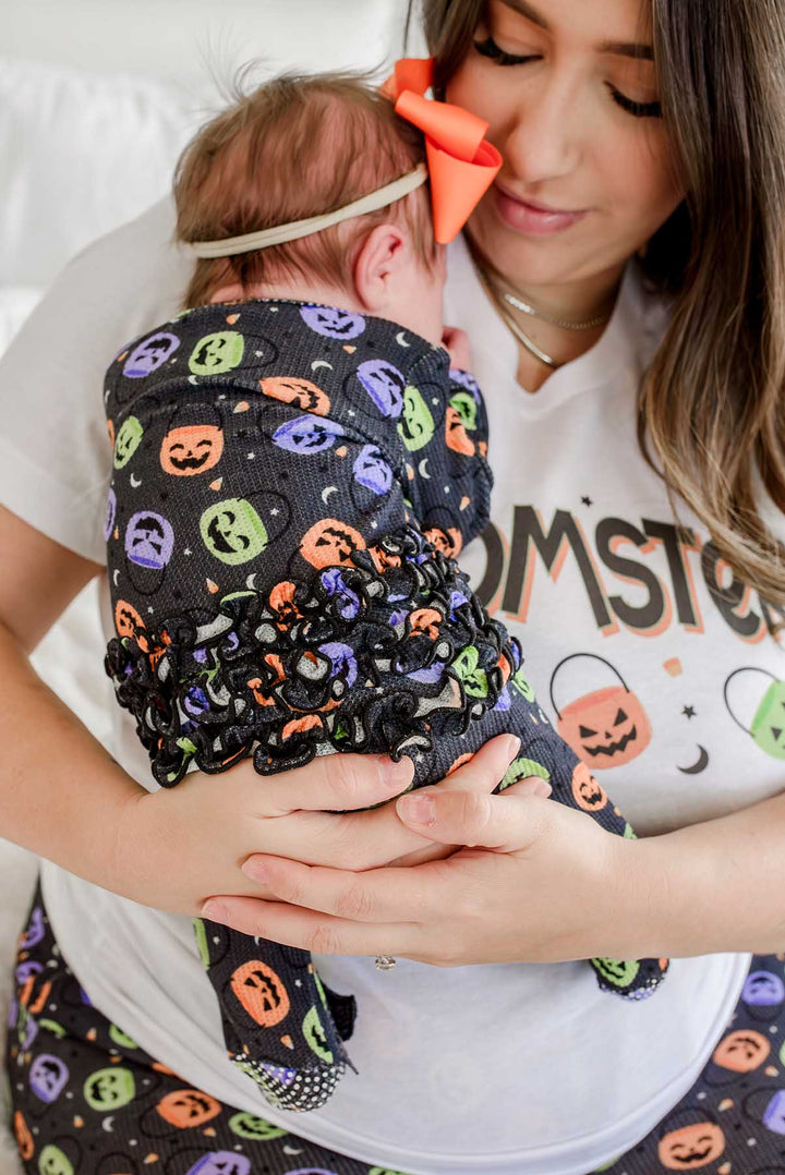 Close-up of mother in 'MOMSTER' t-shirt holding a newborn in an orange bow, wrapped in a candy-print ruffle romper