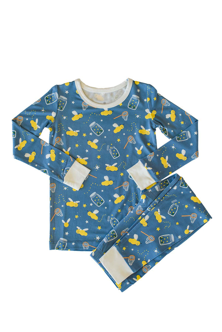 Flat lay of a Caden Lane blue two-piece bamboo pajama set in a Chasing Fireflies print featuring fireflies and mason jars, with sleeves at the sides and folded cream cuffs.