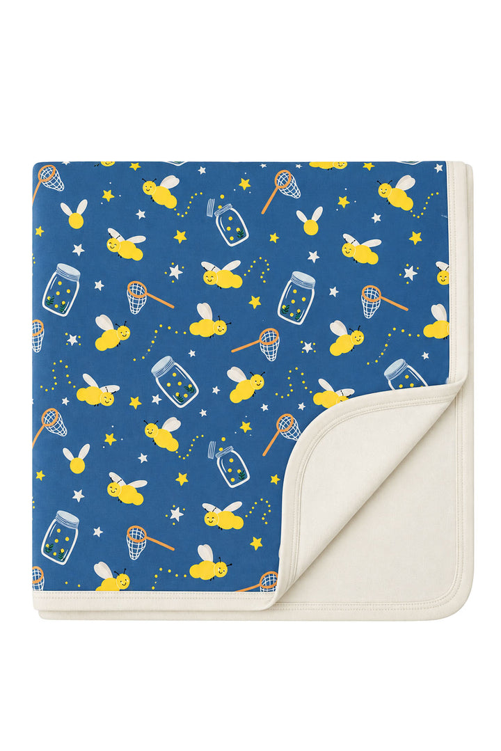 Flat lay of a Caden Lane blue double-sided bamboo blanket in a Chasing Fireflies print featuring fireflies and mason jars, with one corner folded to show the cream reverse.