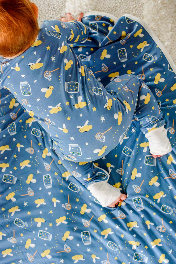 Overhead shot of a baby crawling across a Caden Lane blue double-sided bamboo blanket in a Chasing Fireflies print featuring fireflies and mason jars, paired with a matching romper.