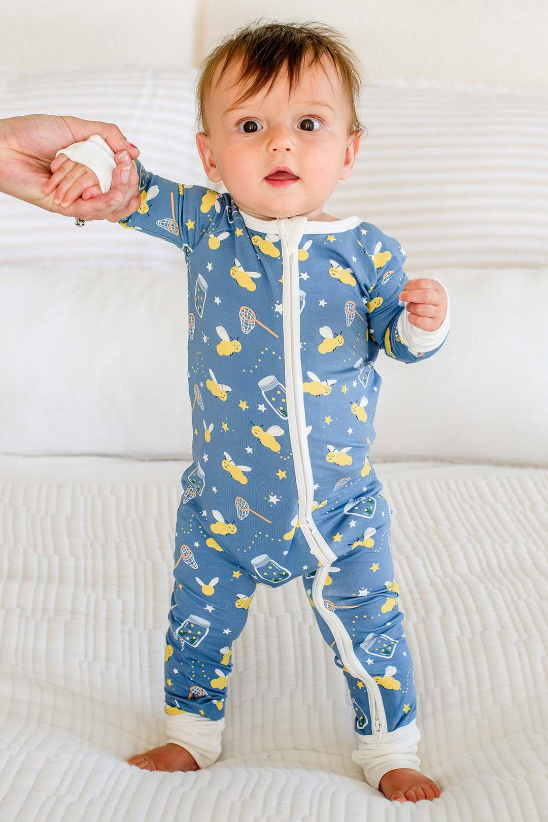 Baby boy standing on a bed holding an adult&