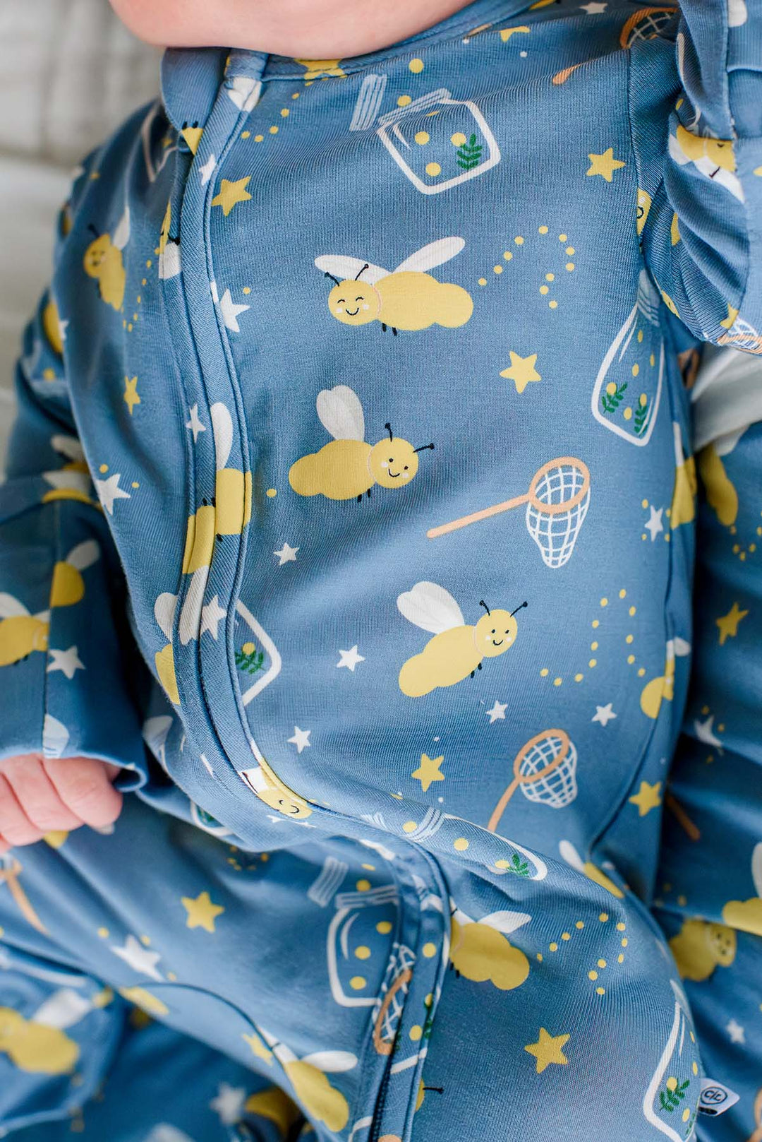 Close-up of the two-way zipper on a Caden Lane blue bamboo zipper footie in a Chasing Fireflies print featuring fireflies and mason jars.