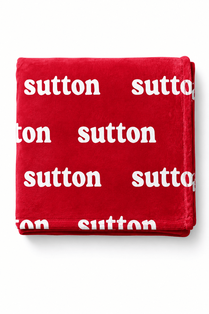 A folded red throw blanket with a repeating white 'sutton' logo print, displayed on a clean white background.
