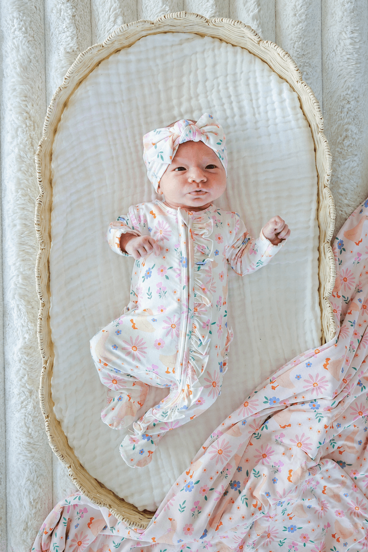 Newborn baby in a bassinet wearing the Lucy Goosy floral print outfit and Knit Large Bow Headwrap, lifestyle overhead photo showing the complete look