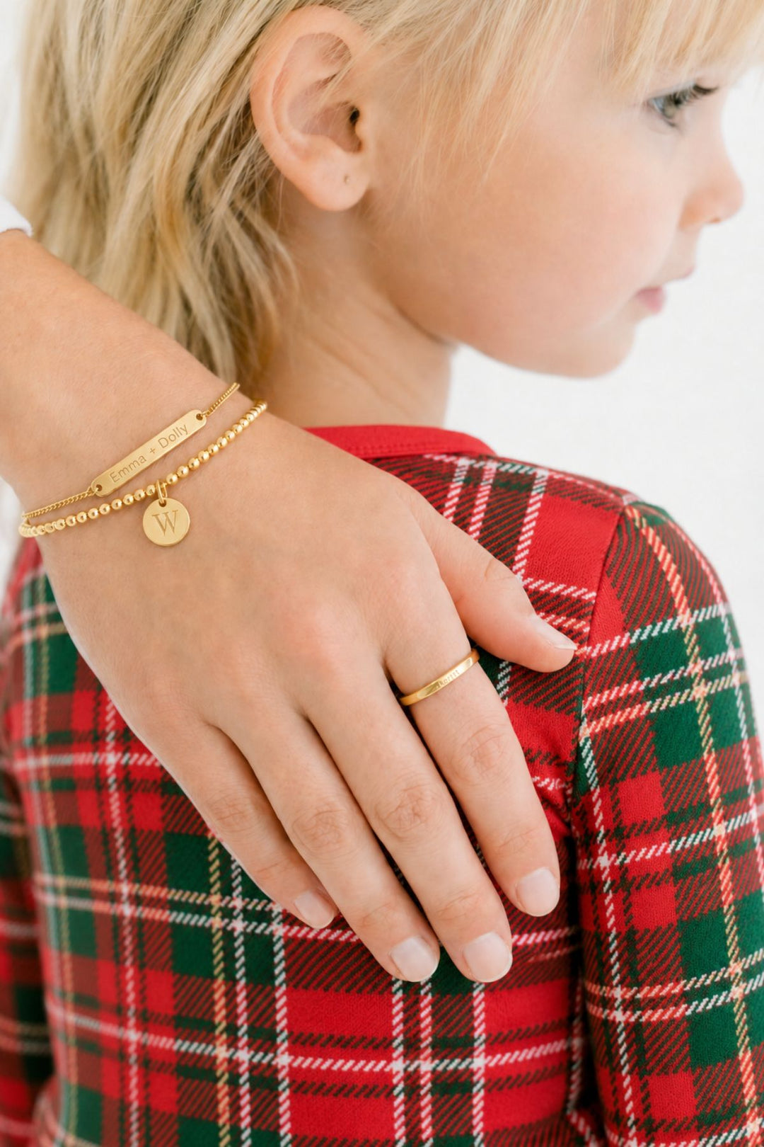Caden Lane gold "Emma + Dolly" engraved bar bracelet, initial "W" disc charm, and matching stackable ring worn by a child in plaid holiday pajamas