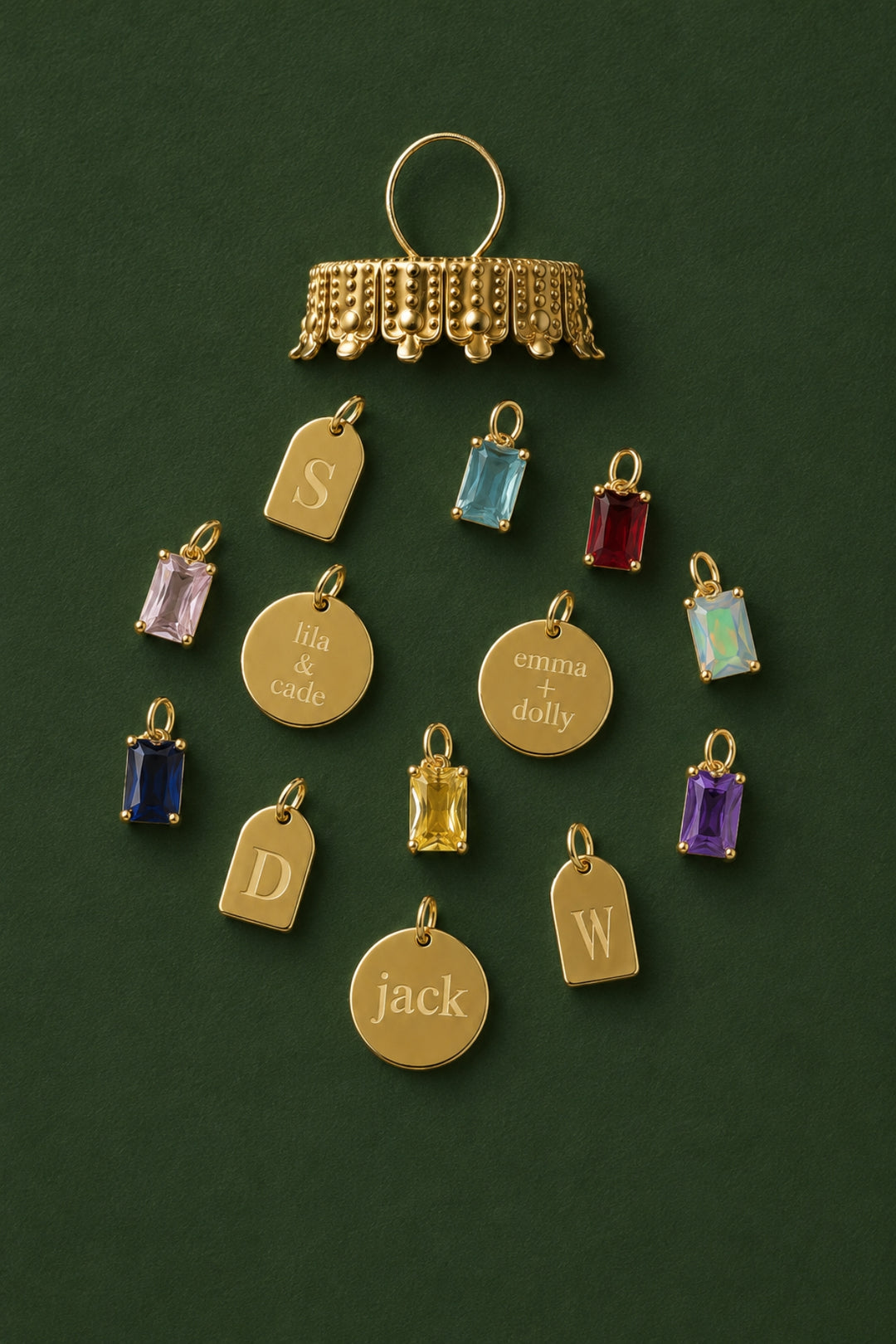 Caden Lane gold charms arranged in a wreath shape, featuring engraved name discs "lila & cade," "emma + dolly," "jack," initial tag charms, and colorful birthstone charms