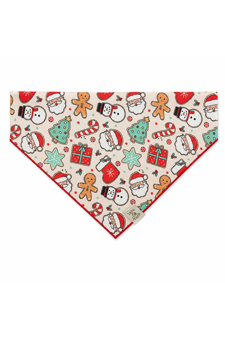 Lane & Leash personalized dog bandana in cream Christmas Treats print with gingerbread men, Santa faces, snowmen, mini trees, candy canes, and gift boxes, tied bandana-style, embroidered with the name 'Trixie' in red