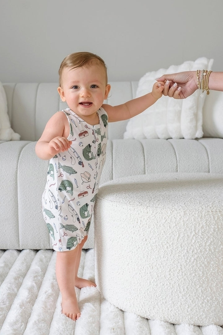 Baby holding parent hand while standing in the Off The Hook sleeveless snap romper side profile view