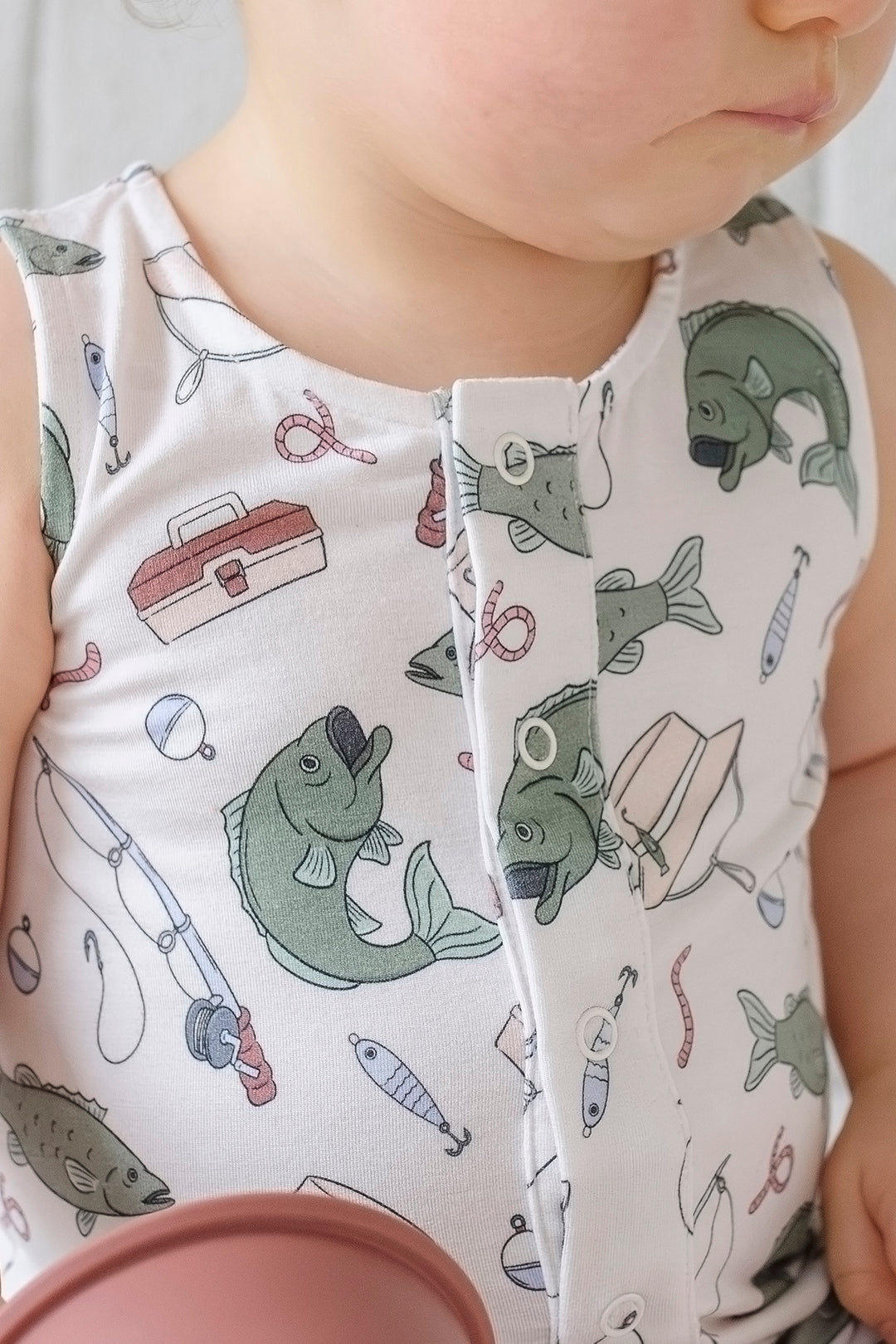 Close-up detail of the Off The Hook sleeveless snap romper fabric showing fishing themed print with fish and tackle