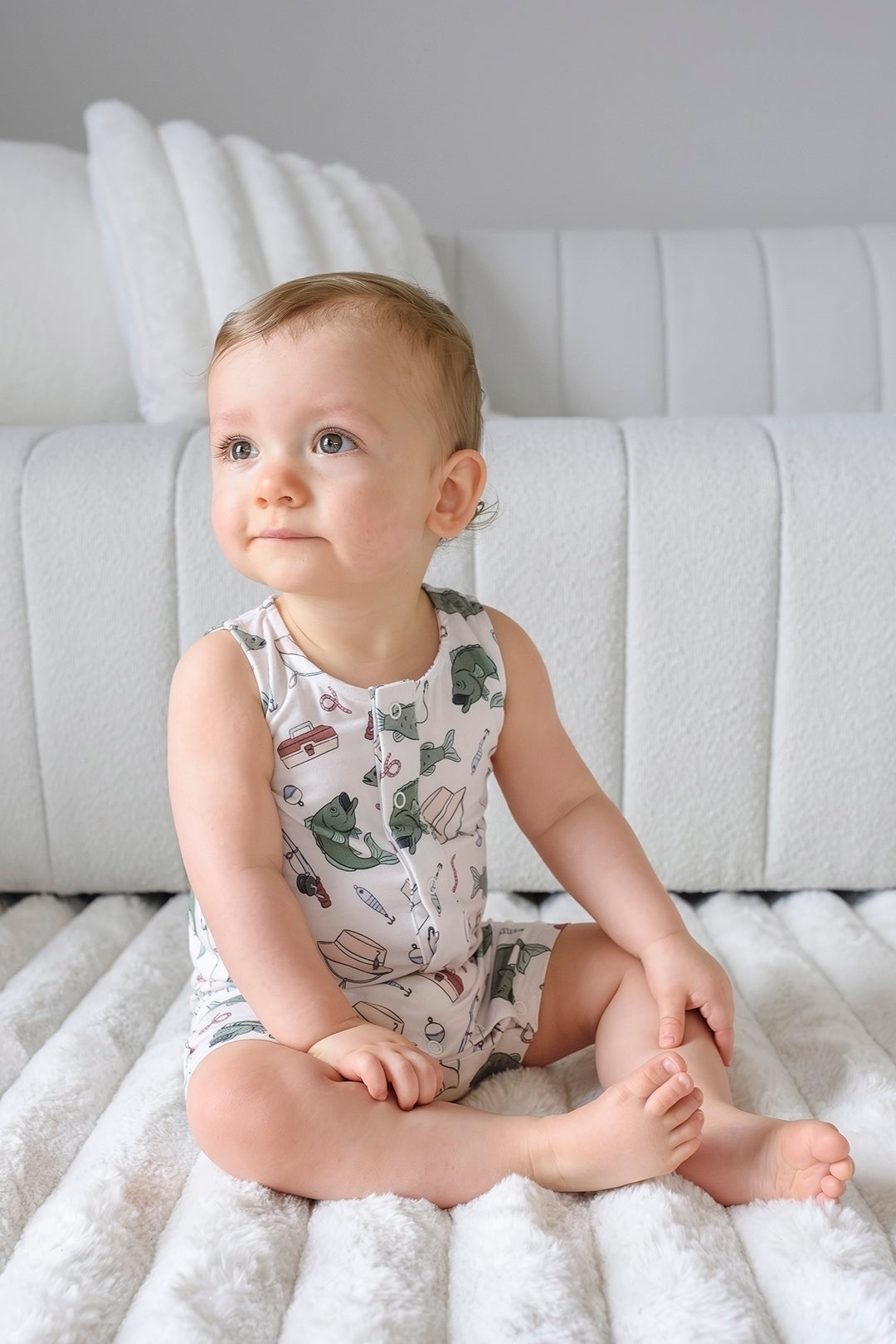 Baby sitting and looking up wearing the Off The Hook sleeveless snap romper with fishing themed print
