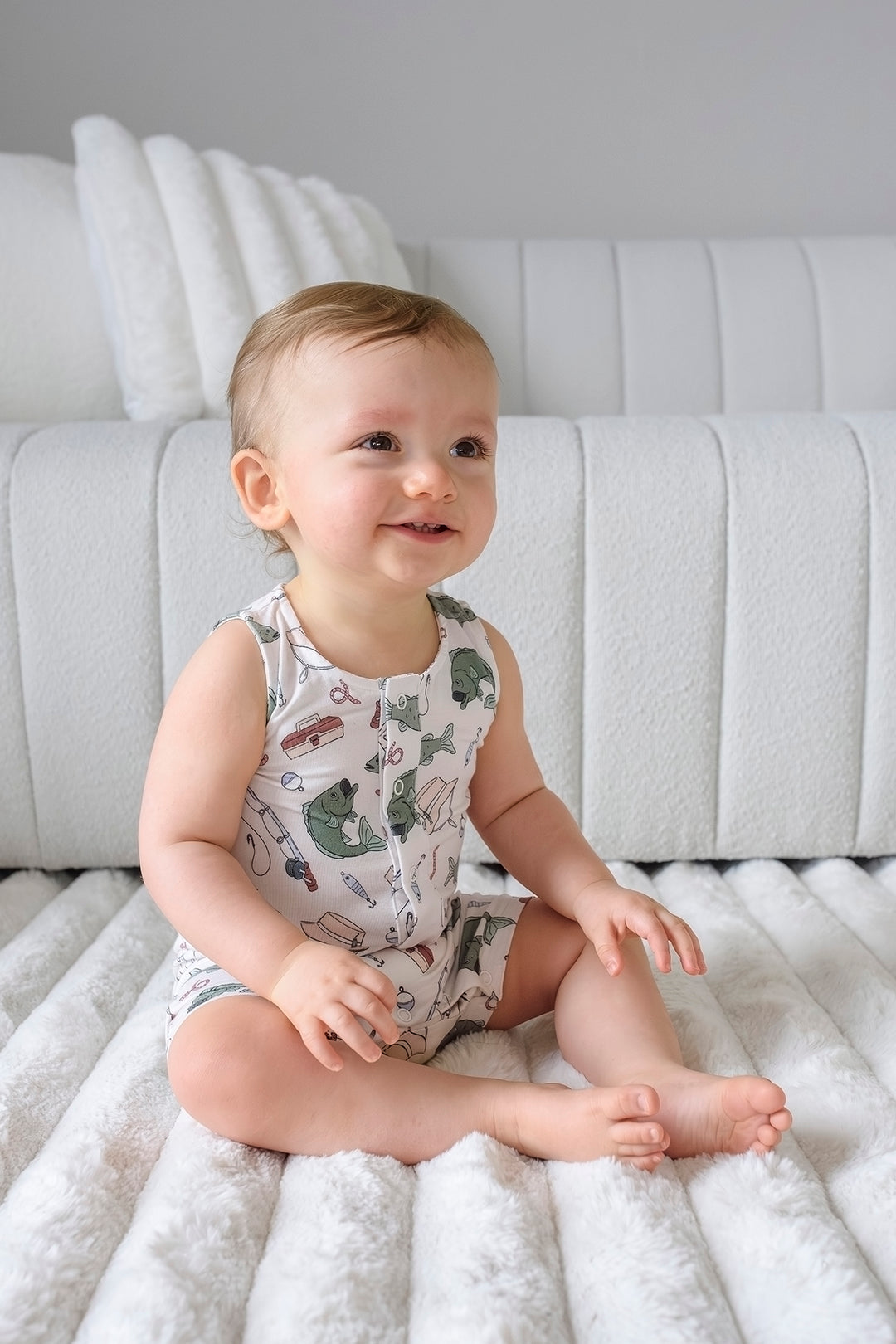 Baby sitting and smiling wearing the Off The Hook sleeveless snap romper with fishing themed print