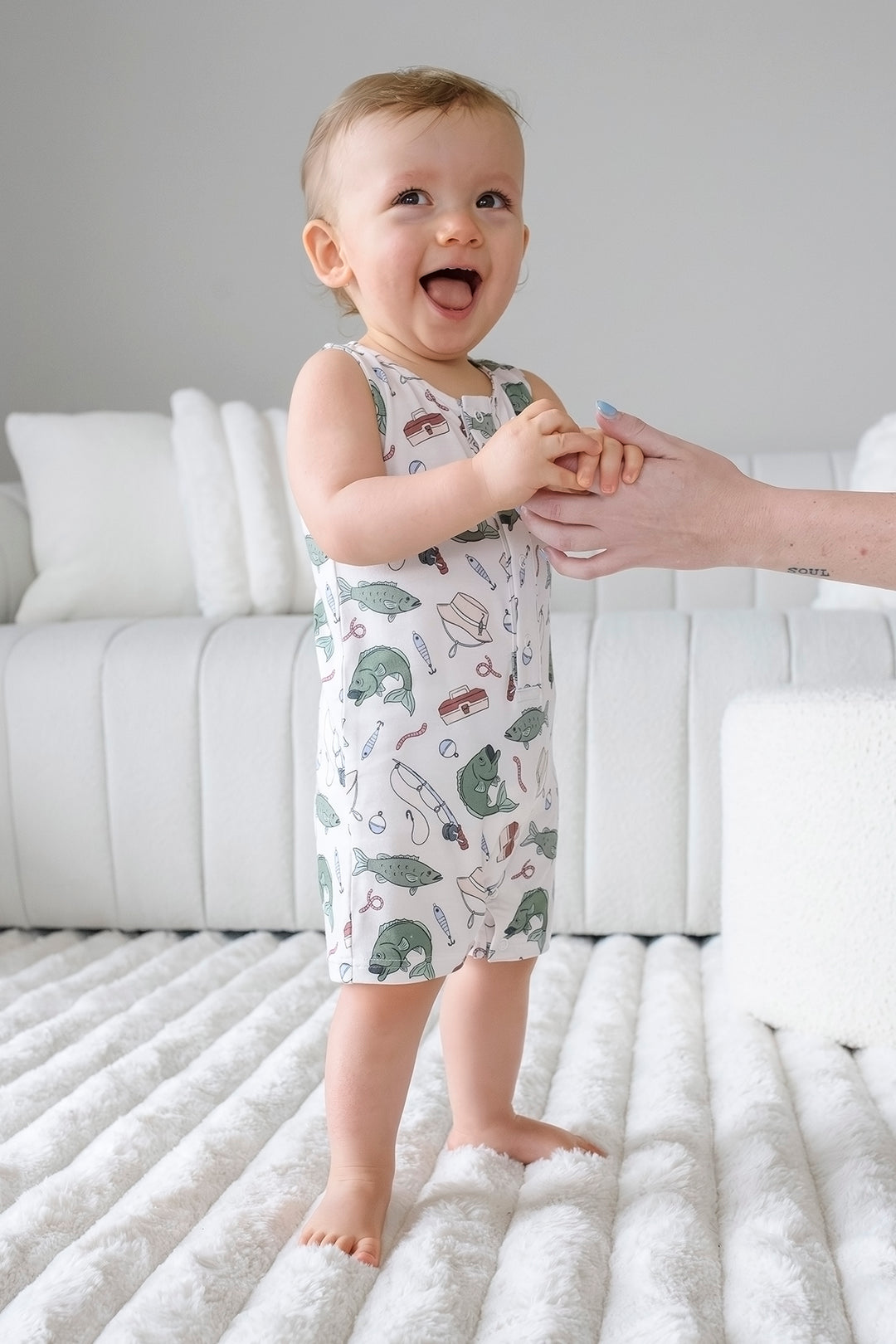 Baby standing and wearing the Off The Hook sleeveless snap romper with fishing themed print