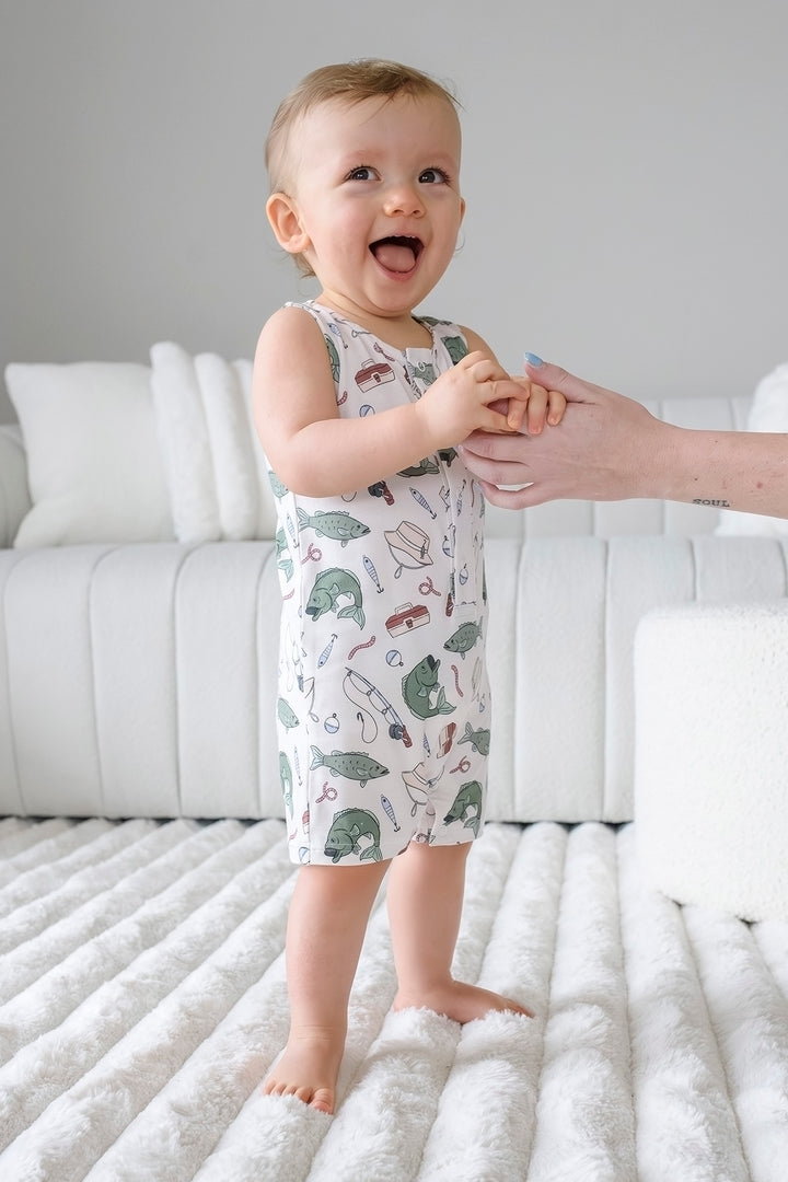 Baby standing and wearing the Off The Hook sleeveless snap romper with fishing themed print