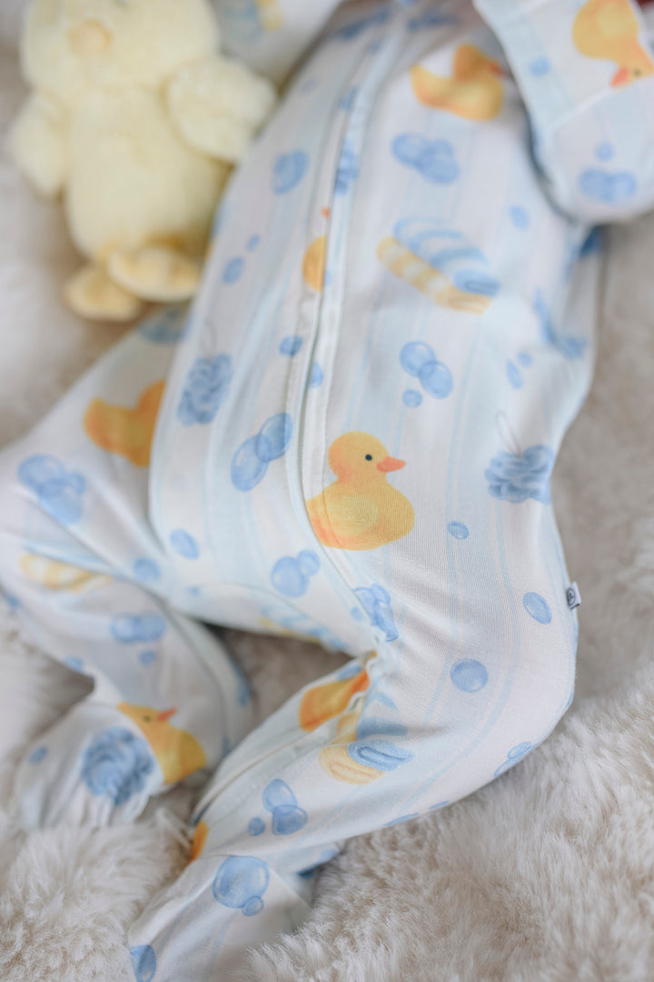 Close-up of newborn's legs in blue Bubble Duckies bamboo zipper footie pajamas with yellow rubber duck stuffed toy