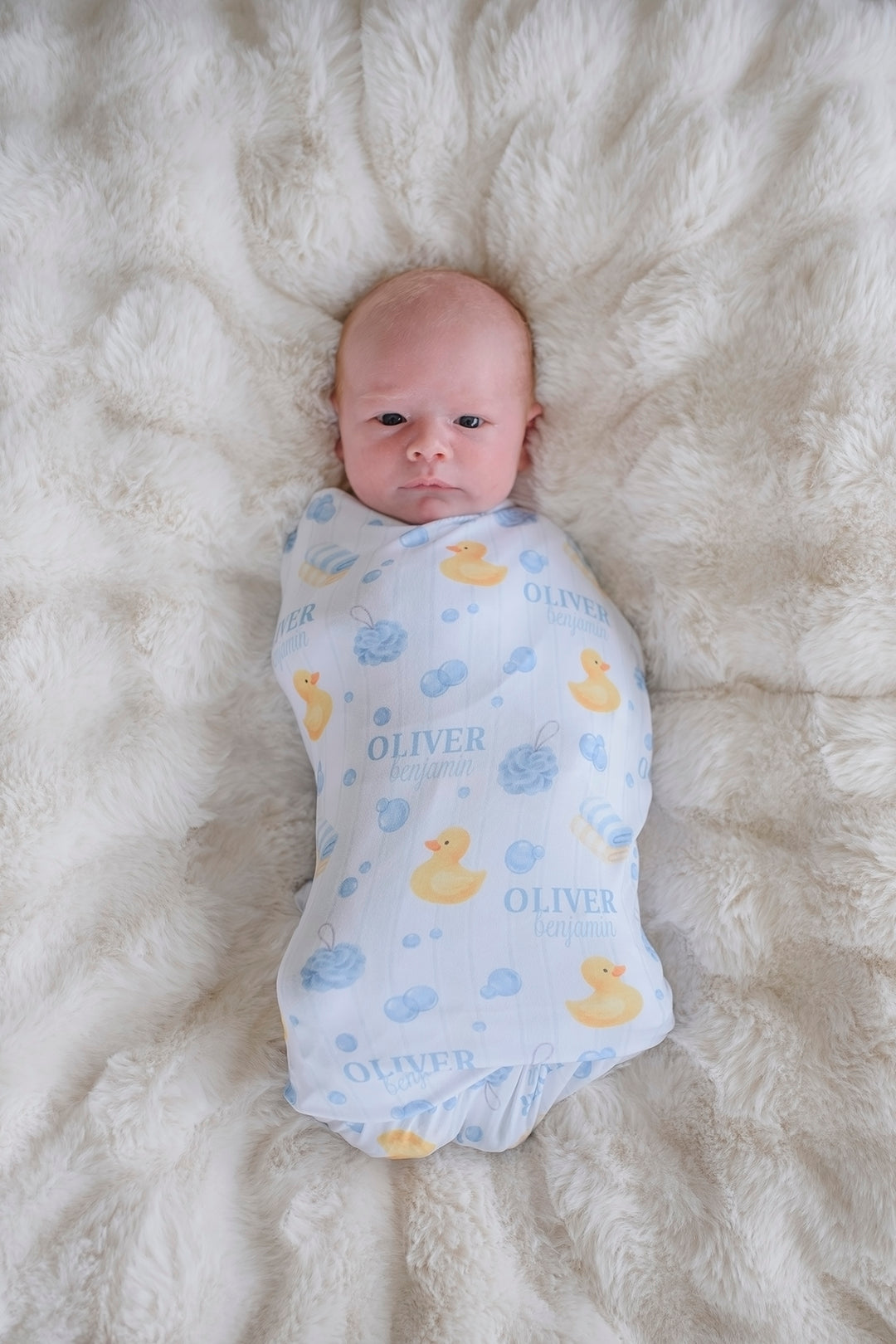 Overhead view of newborn swaddled in blue Bubble Duckies personalized swaddle blanket with rubber duck print