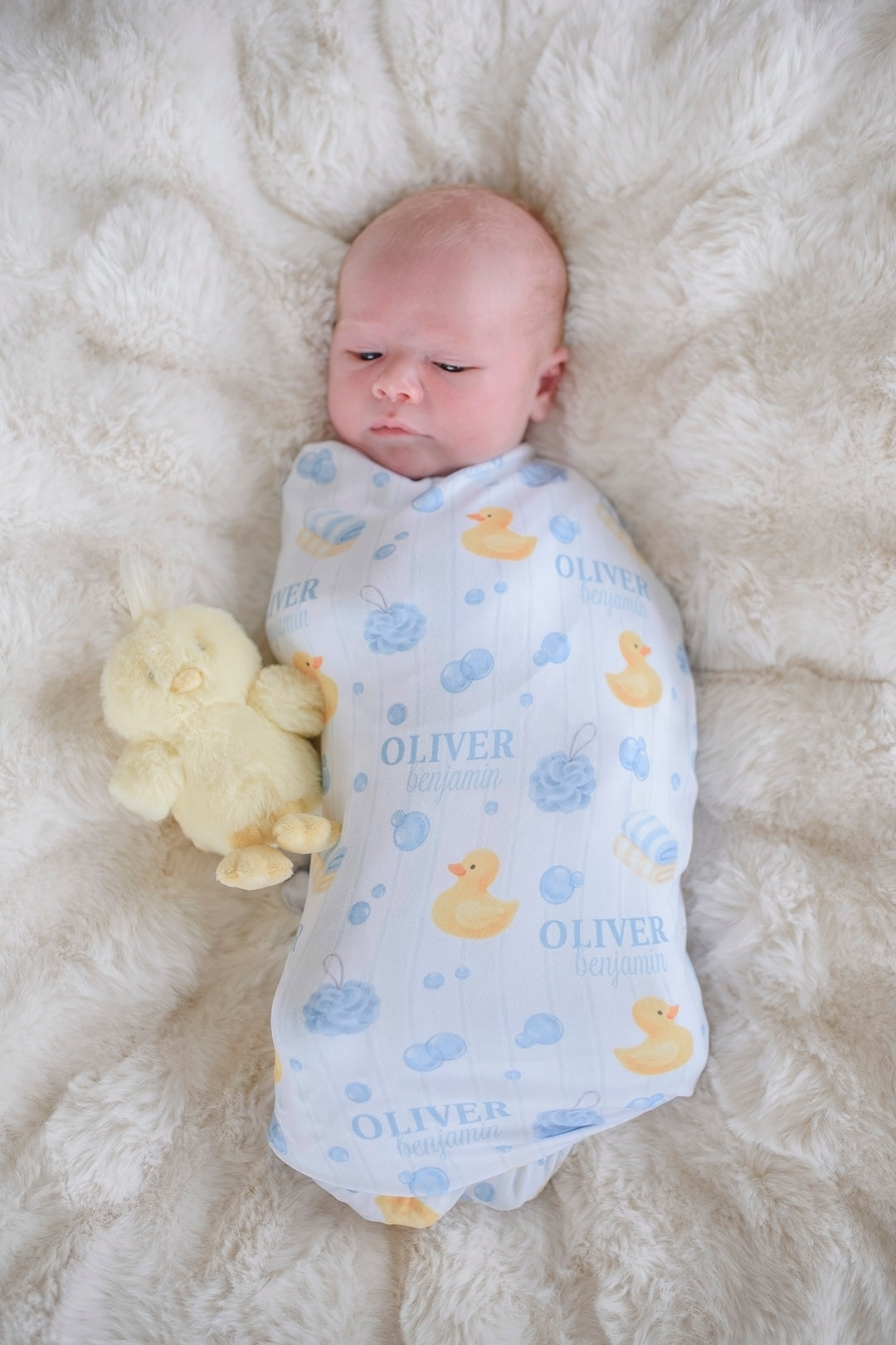 Newborn swaddled in blue Bubble Duckies personalized swaddle blanket with yellow rubber duck print and custom name