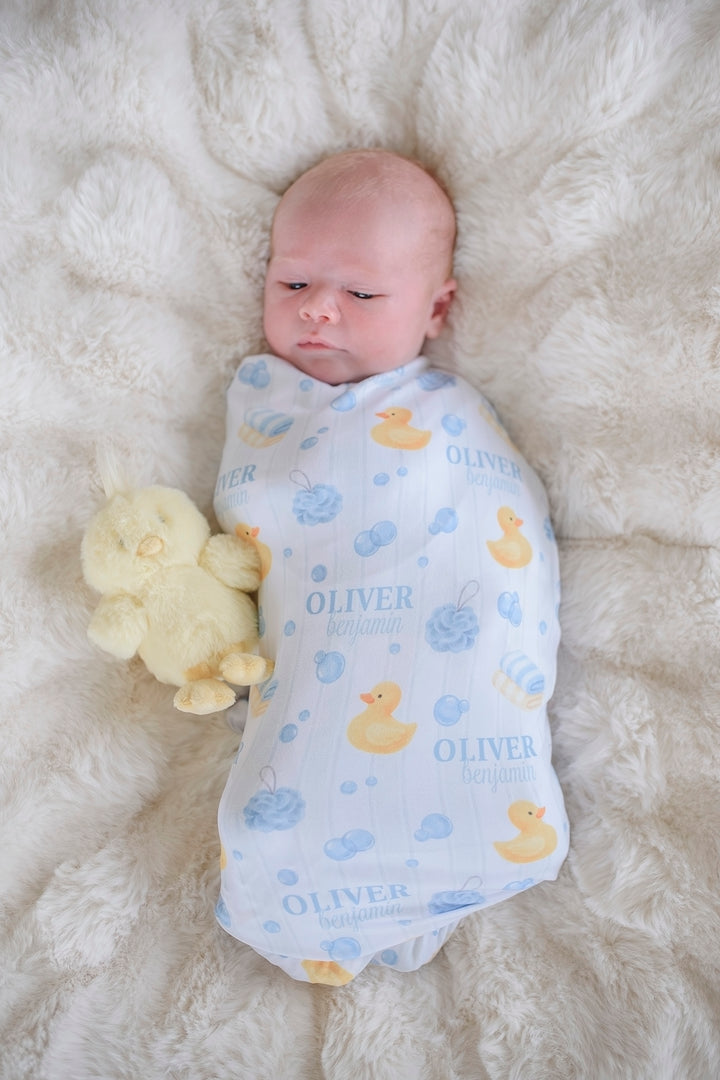 Newborn swaddled in blue Bubble Duckies personalized swaddle blanket with yellow rubber duck print and custom name