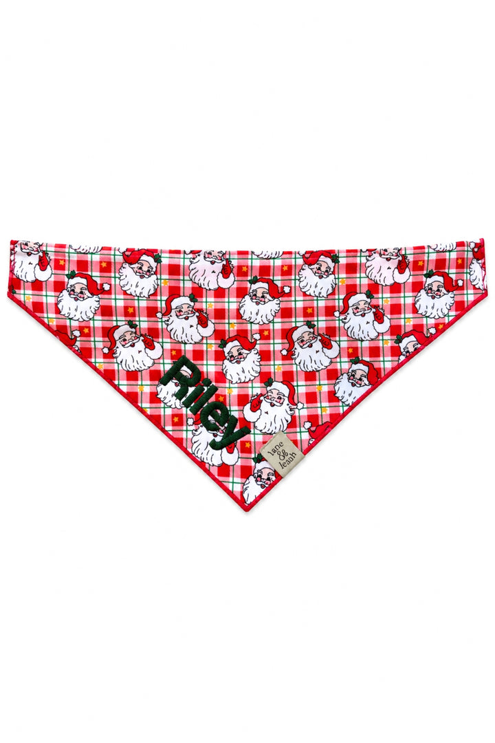 Lane & Leash personalized dog bandana in red plaid Cozy Claus print with vintage Santa Claus faces, tied bandana-style, embroidered with the name 'Riley' in green