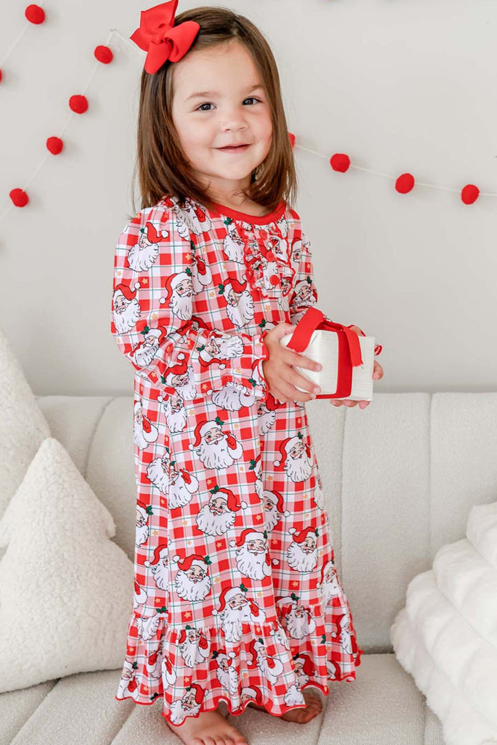 Toddler girl wearing a Caden Lane Cozy Claus Christmas princess ruffle nightgown featuring a vintage Santa plaid print while holding a wrapped holiday gift.