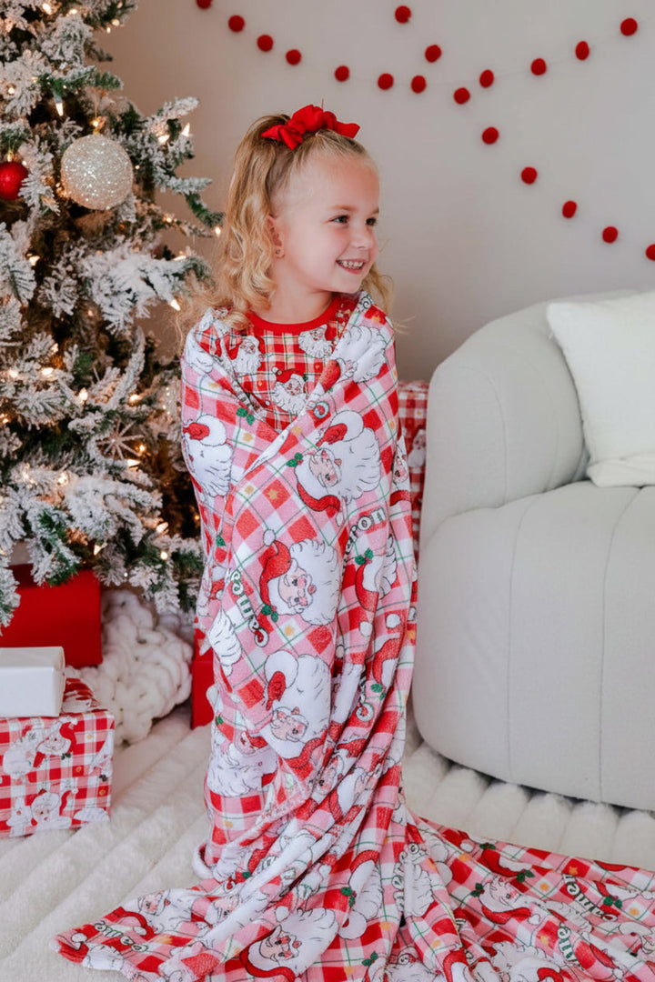 Toddler wrapped in a personalized Cozy Claus Christmas blanket with a vintage Santa print, creating cozy holiday memories by the Christmas tree.