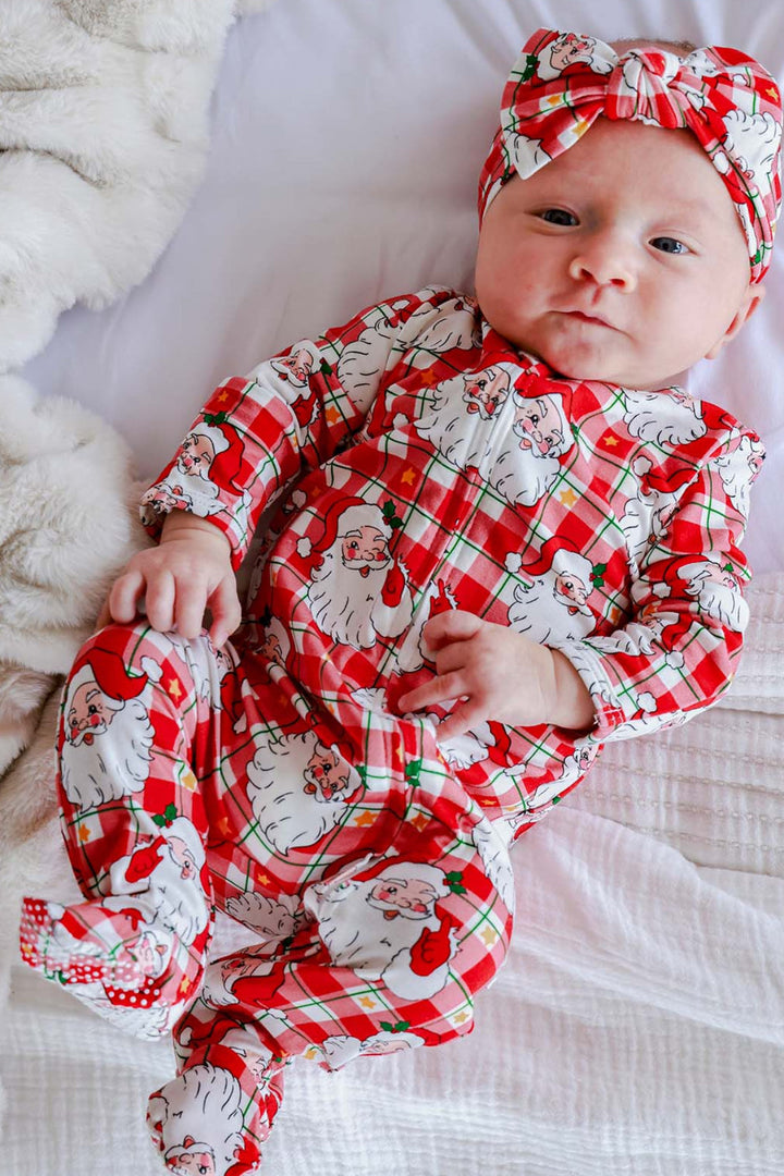 Baby wearing a Caden Lane Cozy Claus Christmas bamboo zipper footie and matching oversized bow headwrap featuring a vintage Santa plaid print for festive holiday style.