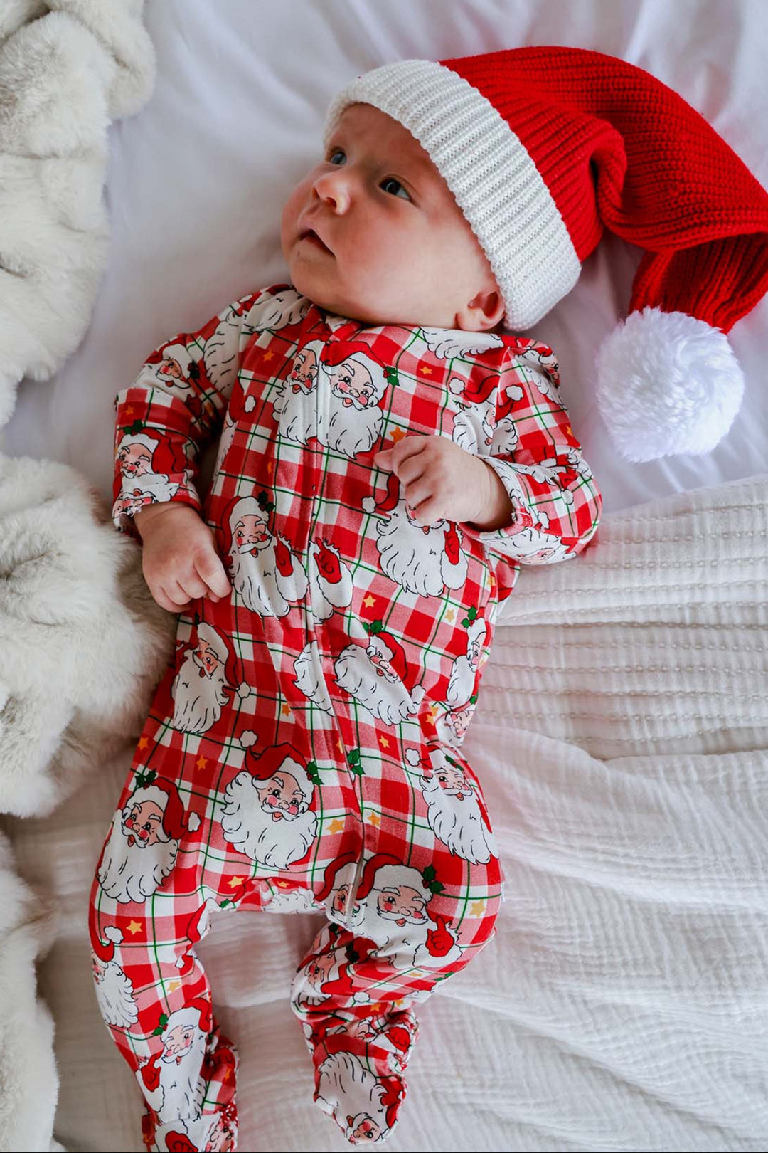 Baby wearing a Caden Lane Cozy Claus Christmas bamboo zipper footie in a vintage Santa plaid print with a classic red Santa hat for holiday photos.