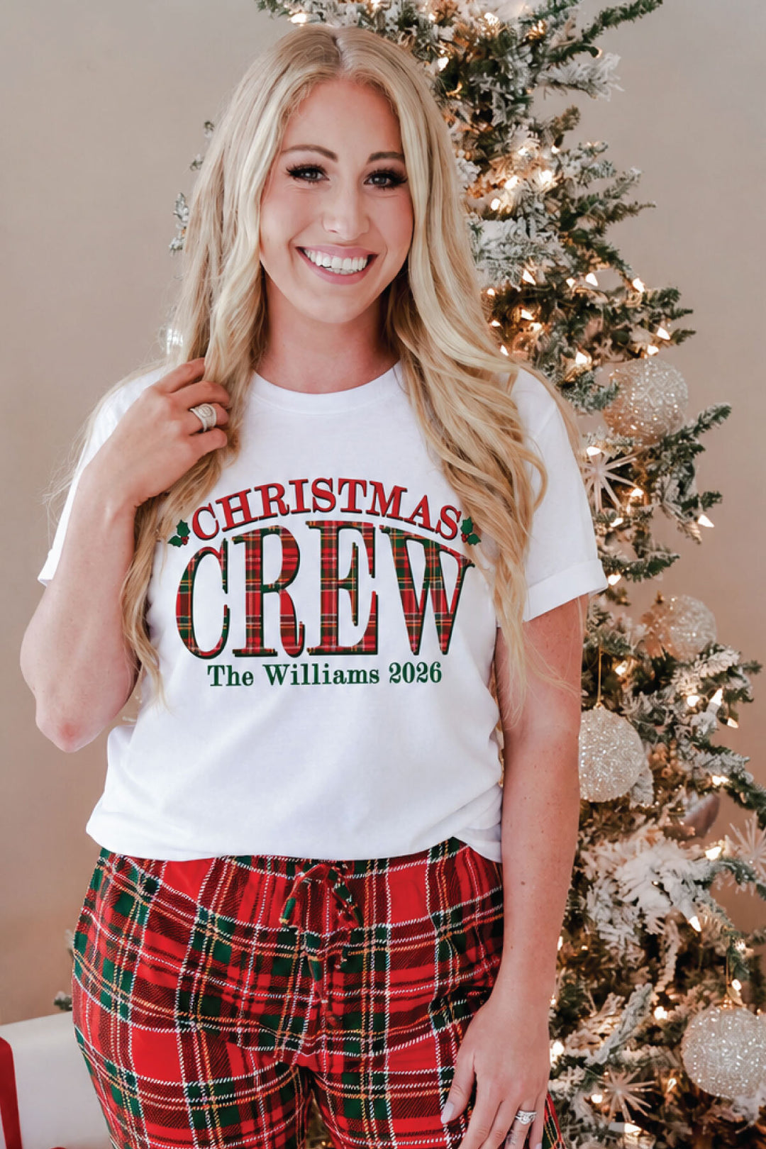 A smiling woman wearing Caden Lane personalized "Christmas Crew" graphic tee featuring a custom family name and year in festive plaid lettering.