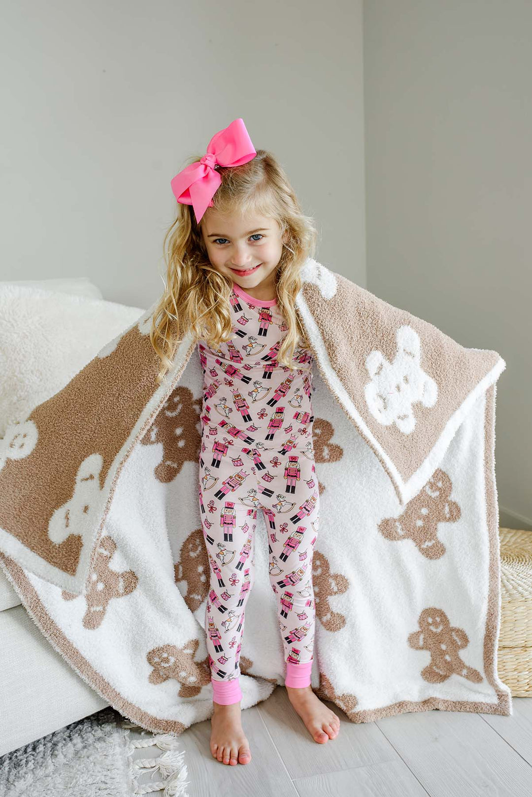 Young girl in pink nutcracker print pajamas wrapped in a Caden Lane taupe and white gingerbread man print sherpa blanket."