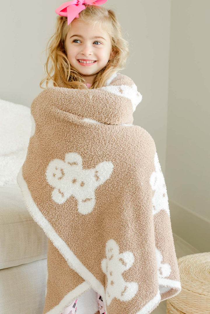 Smiling girl wrapped up in a Caden Lane taupe gingerbread man print sherpa blanket, shown from the back with the allover gingerbread pattern visible