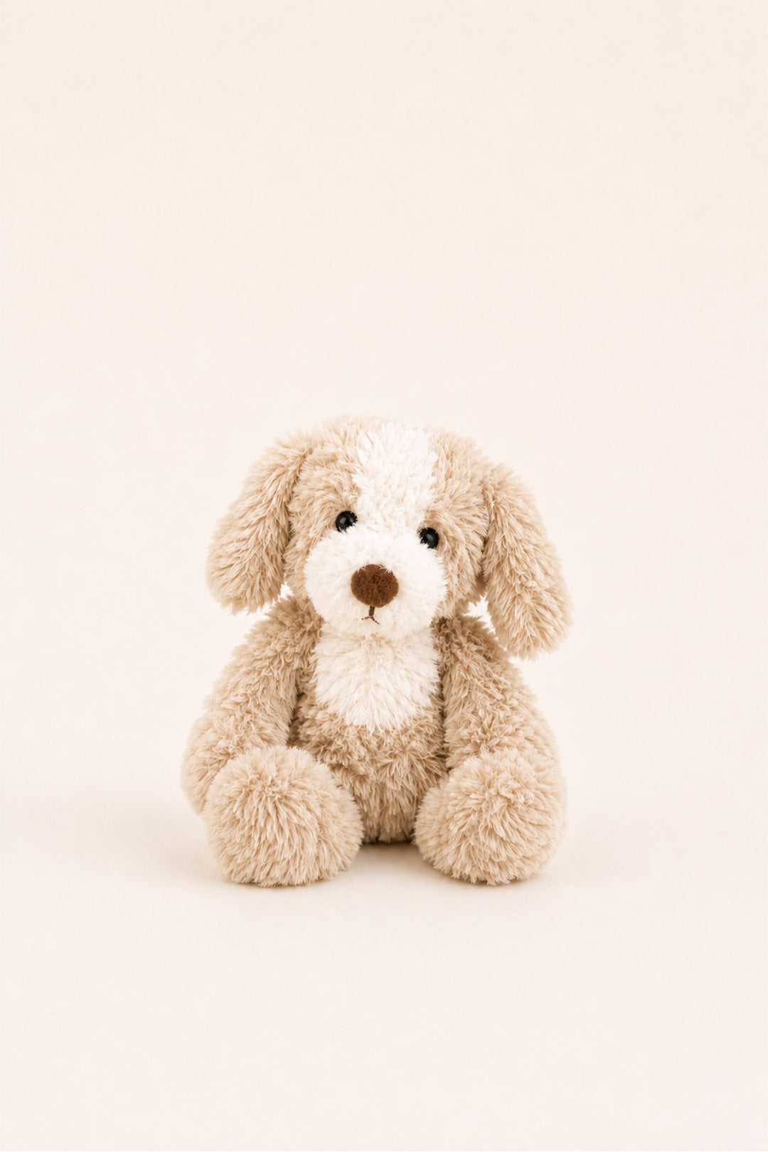 A Caden Lane plush stuffed dog toy in light beige and cream with a brown nose, sitting centered against a plain warm off-white background.