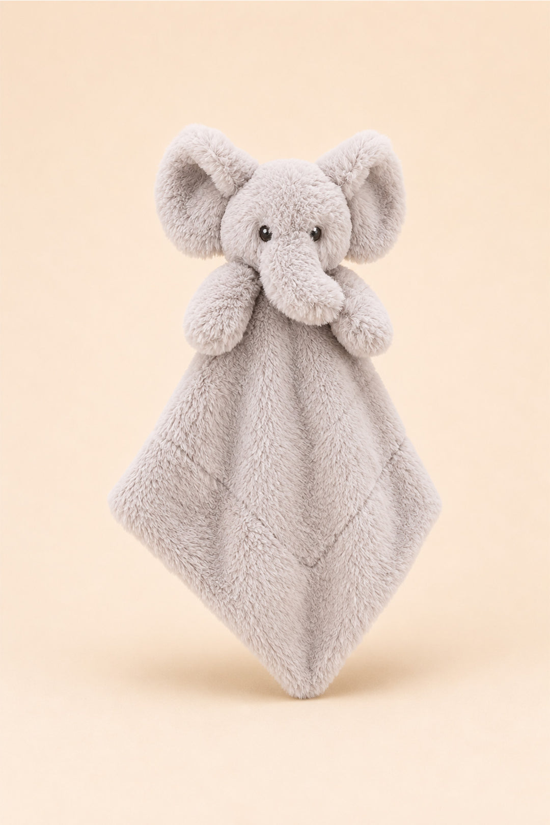 A Caden Lane light gray plush elephant security blanket with a soft diamond-shaped fabric body, photographed against a solid pale peach background.