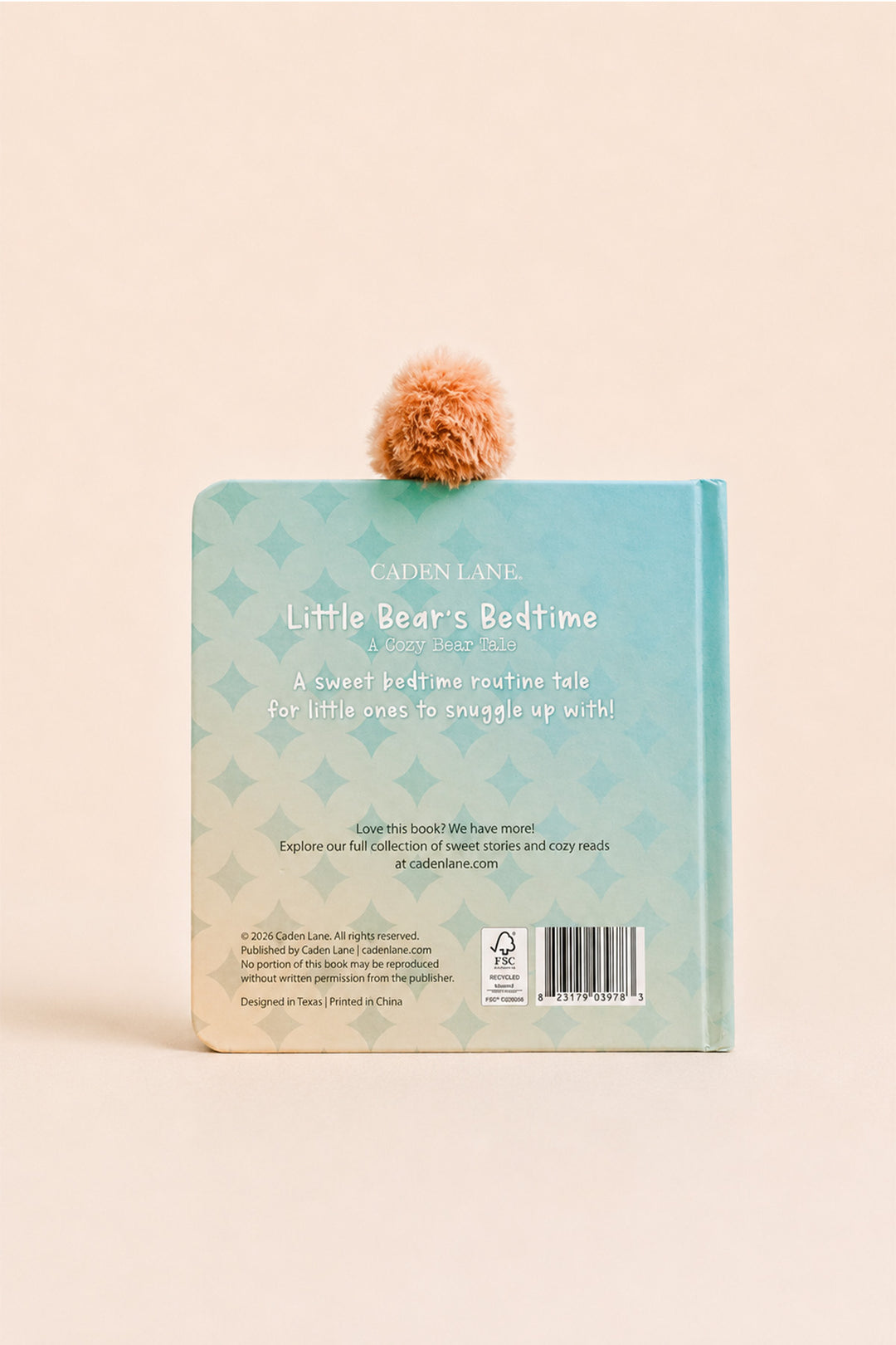 The back cover of a children's book titled 'Little Bear's Bedtime' by Cadence Lane, featuring a light blue and mint green patterned cover with a fluffy peach pom-pom attached at the top, set against a solid pale peach background.