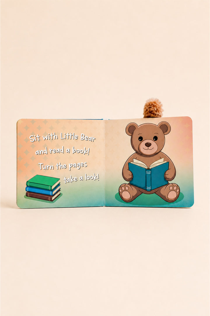 An open children's book with a small pom-pom tail at the top, showing a teddy bear reading a blue book on the right page and the text 'Sit with Little Bear and read a book! Turn the pages take a look!' on the left page, set against a warm cream background.
