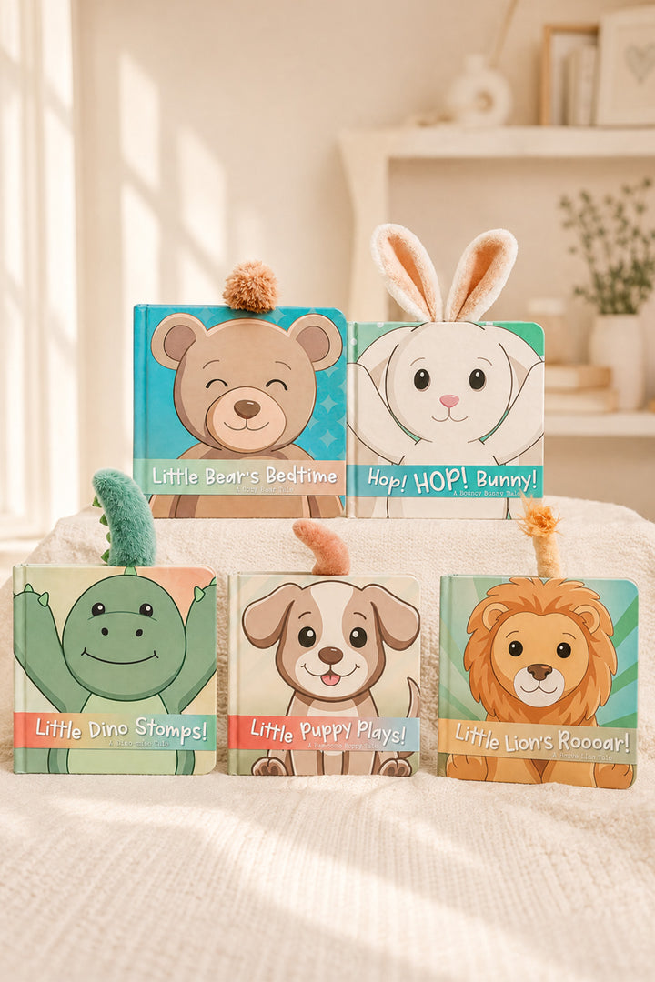 Five children's wooden board books with animal illustrations are arranged on a soft cream fabric surface in a bright, warm room. The books feature cartoon bear, bunny, dinosaur, puppy, and lion covers with colorful pastel backgrounds.