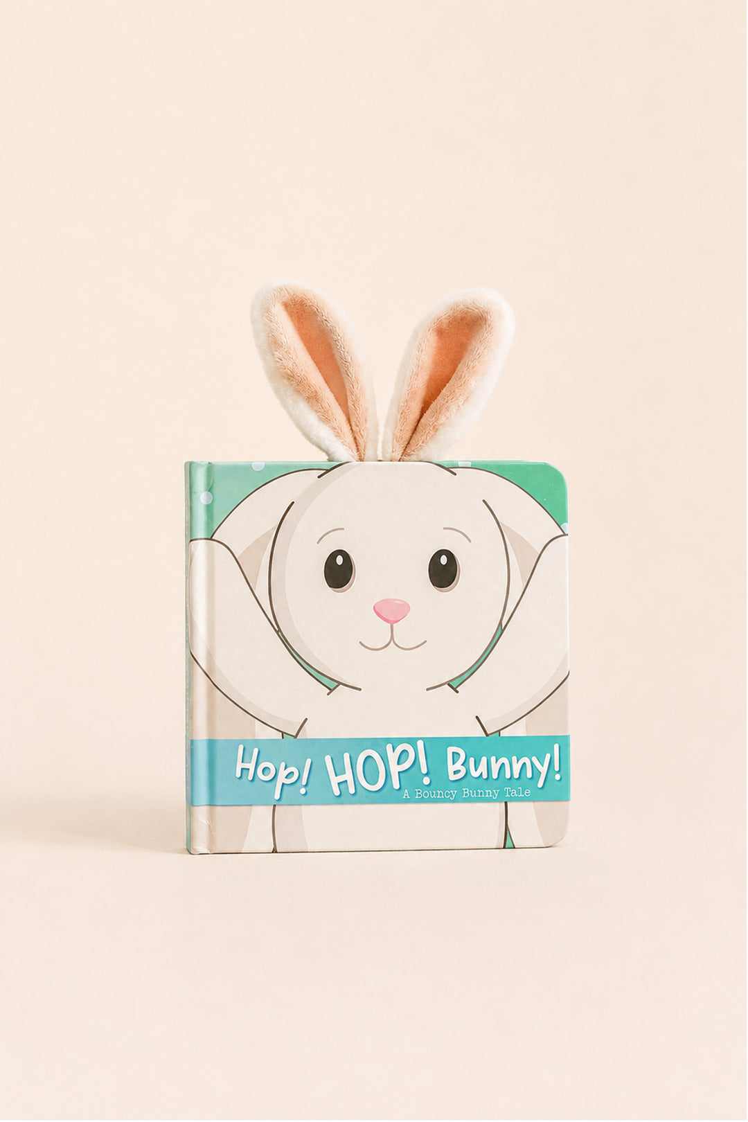 A children's board book titled 'Hop! HOP! Bunny!' featuring a white bunny illustration with pink details and soft peach-tinted bunny ears sticking out from the top, set against a solid pale beige background.