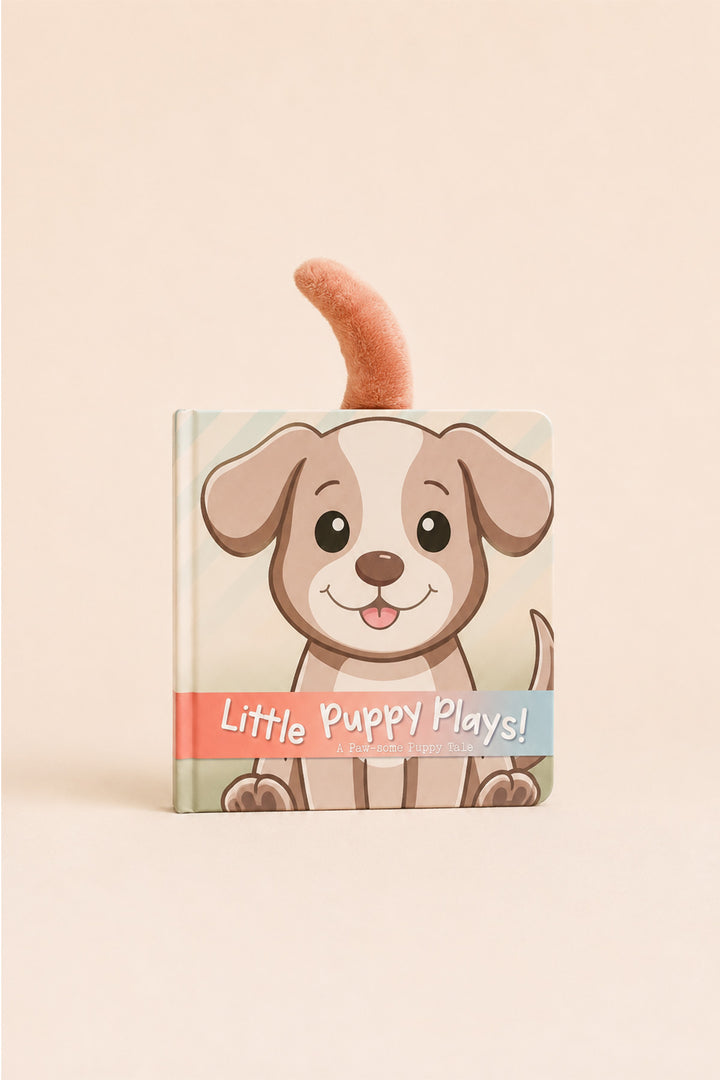 A children's hardcover book titled 'Little Puppy Plays!' featuring a cute cartoon puppy illustration on the cover and a plush toy tail attached to the top, set against a solid light beige background.