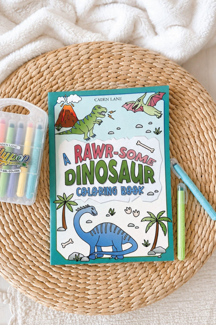 Caden Lane "A Rawr-Some Dinosaur" coloring book featuring dinosaurs and a volcano, styled with Gellypop gel crayons on a woven tray.