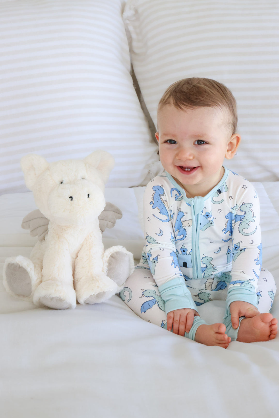 smiling baby boy in blue dragon pajamas next to a white dragon stuffed animal 