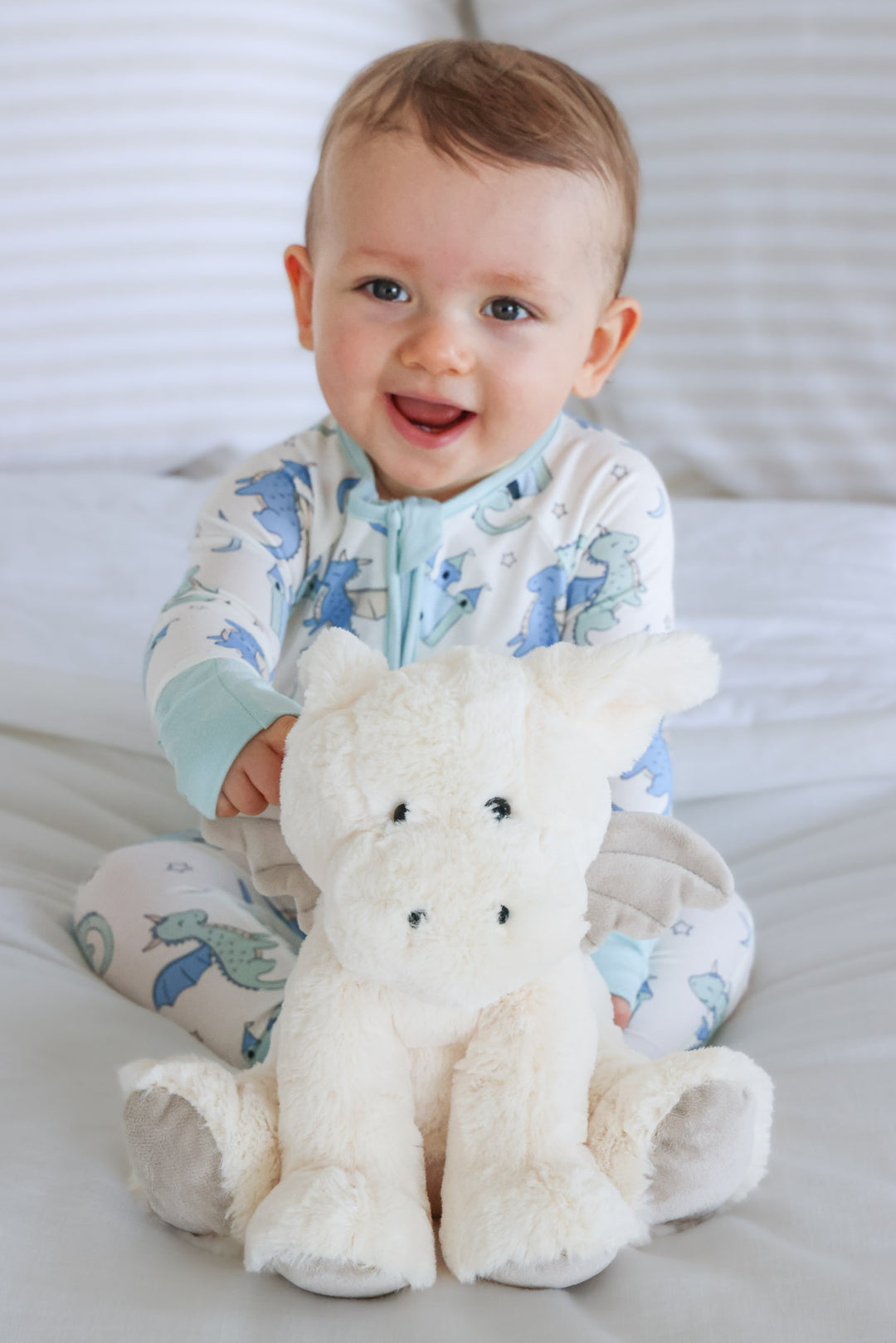 happy baby boy holding a white dragon stuffed animal 