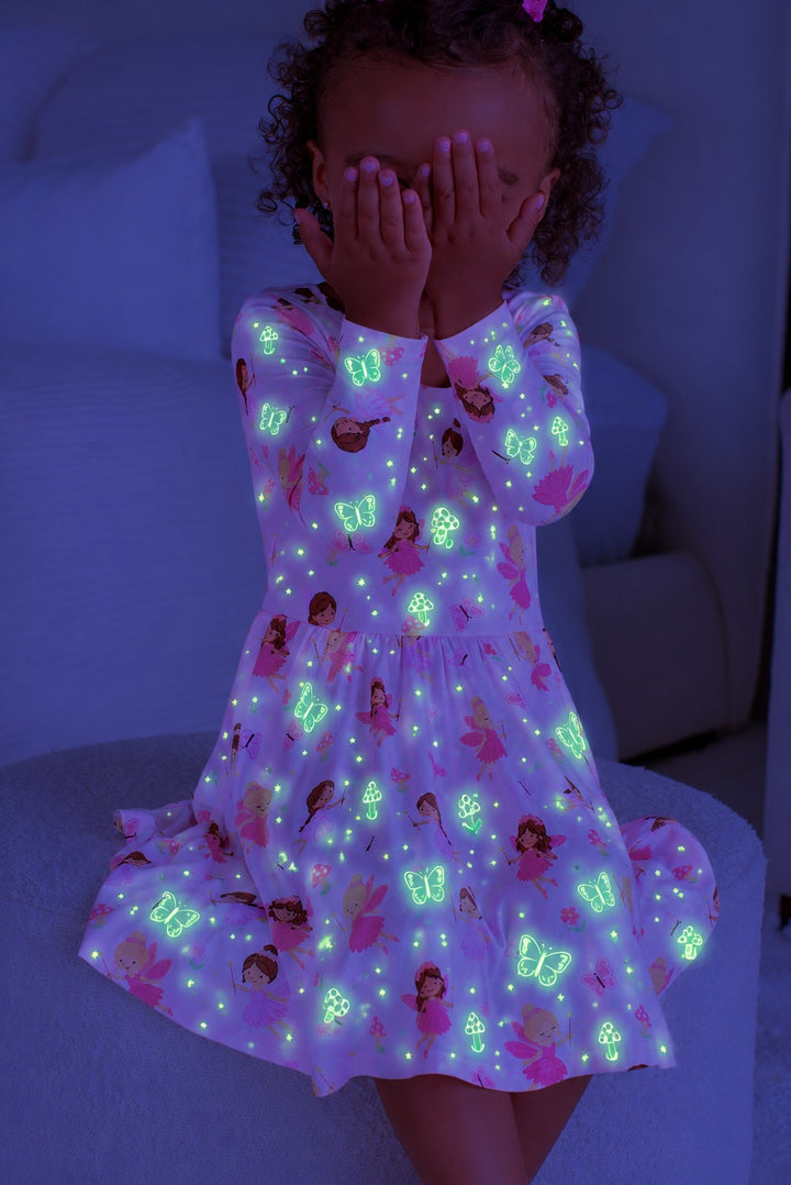 Girl covering her face with both hands, wearing a glowing Caden Lane pink bamboo long sleeve twirl dress in a Fairy Wishes print featuring fairies and butterflies.