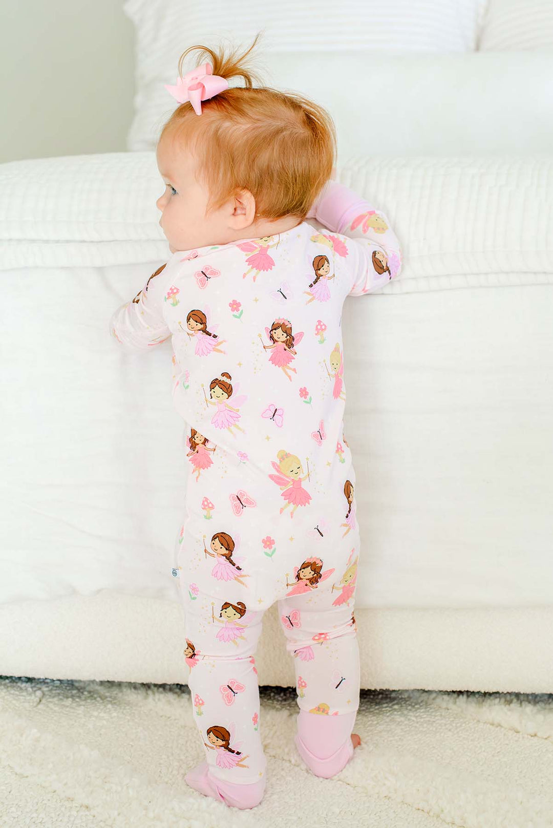 Baby standing at the bed in the Fairy Wishes glow-in-the-dark convertible bamboo zip romper with feet folded over