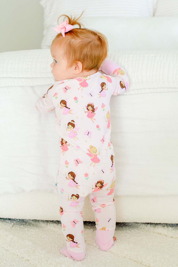 Baby standing at the bed in the Fairy Wishes glow-in-the-dark convertible bamboo zip romper with feet folded over