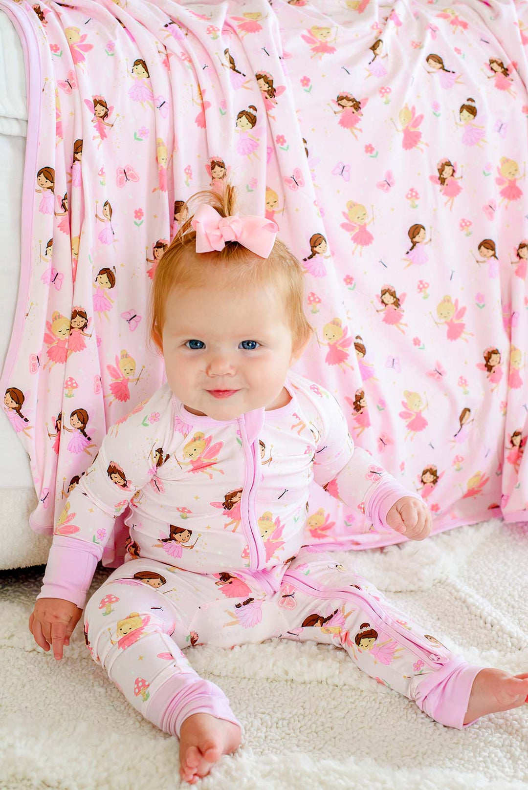 Baby in a matching Fairy Wishes fairy print romper sitting in front of the Fairy Wishes glow-in-the-dark double-sided bamboo blanket
