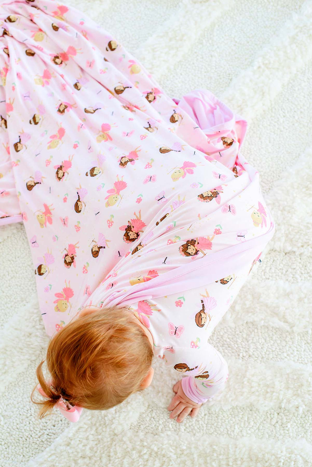Baby crawling on a rug with the Fairy Wishes glow-in-the-dark double-sided bamboo blanket draped over her back