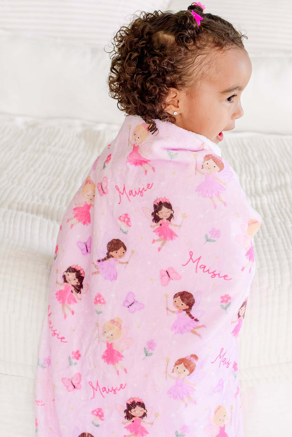 Side view of a toddler wrapped in the Fairy Wishes personalized kids' blanket showing pink fairies, butterflies and custom name print