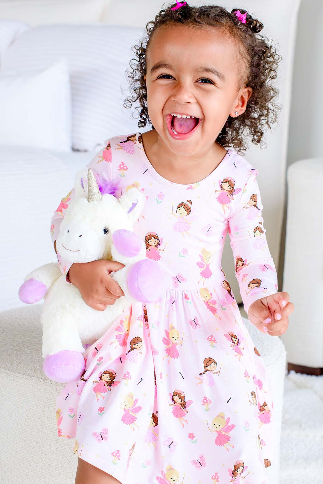 Laughing toddler girl in the Fairy Wishes long sleeve twirl dress holding a plush unicorn