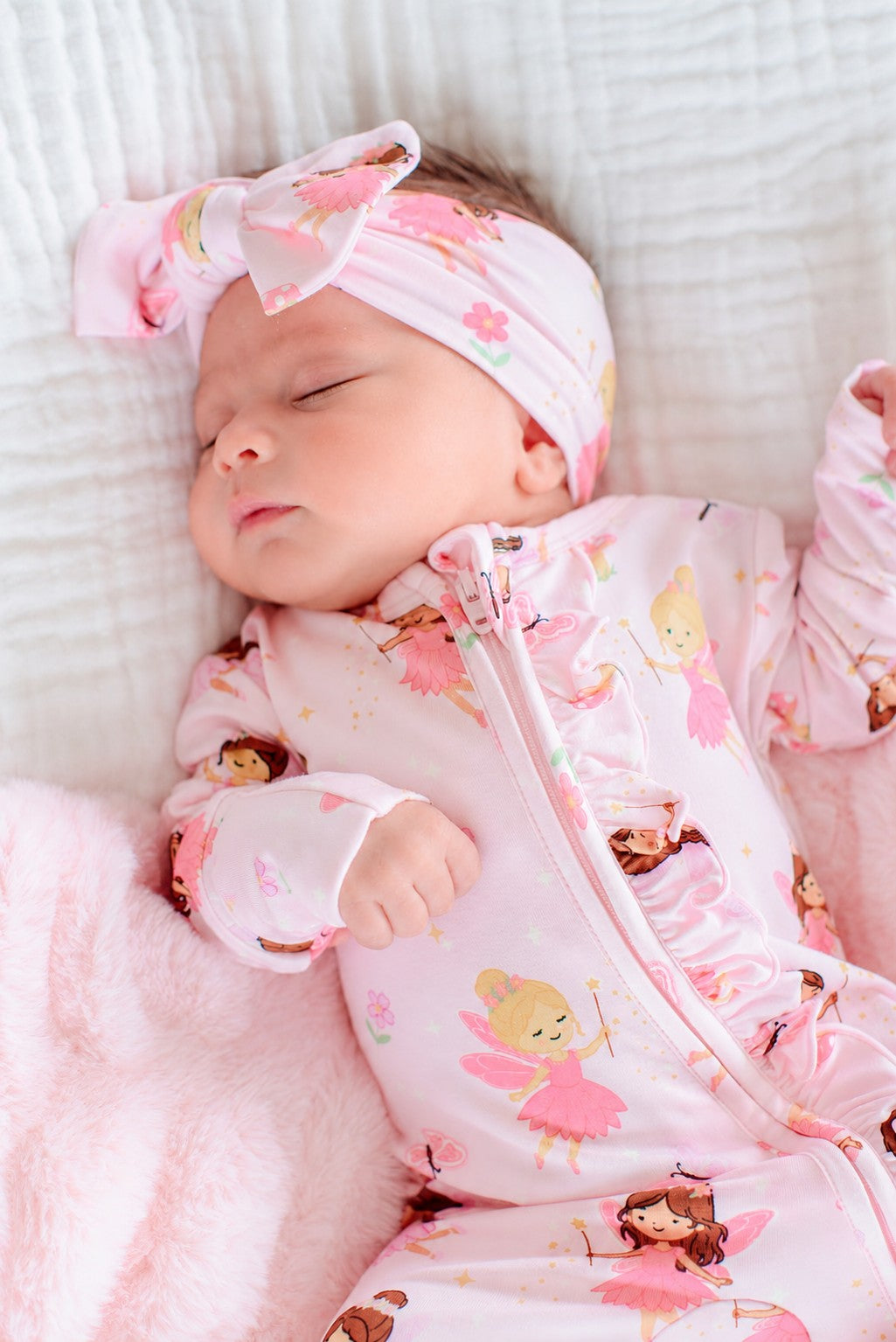 Close-up of a newborn in the Fairy Wishes glow-in-the-dark zipper ruffle footie and matching fairy print bow headwrap